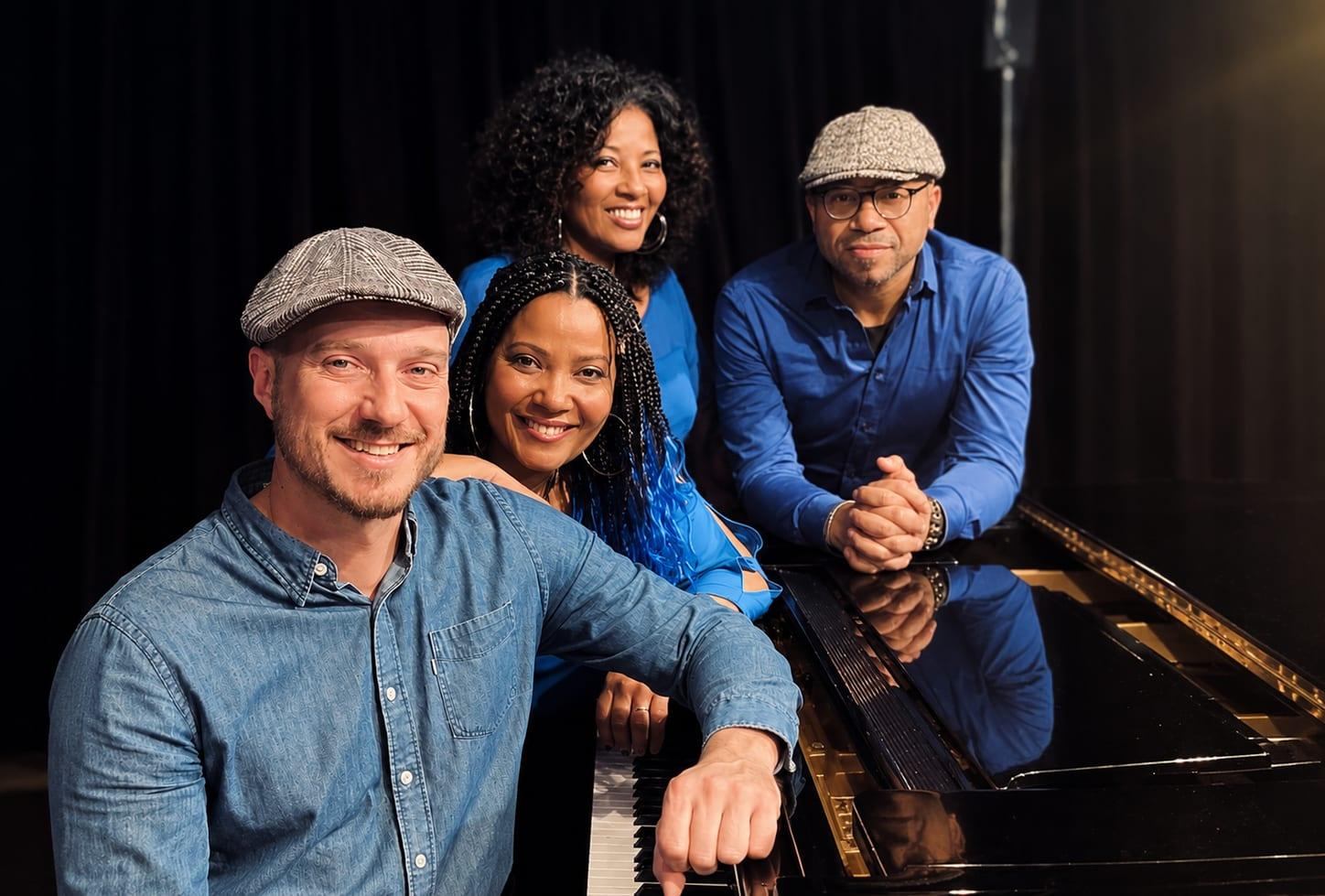 Les quatre chanteurs réunis autour d’un piano à queue, en chemises bleues.