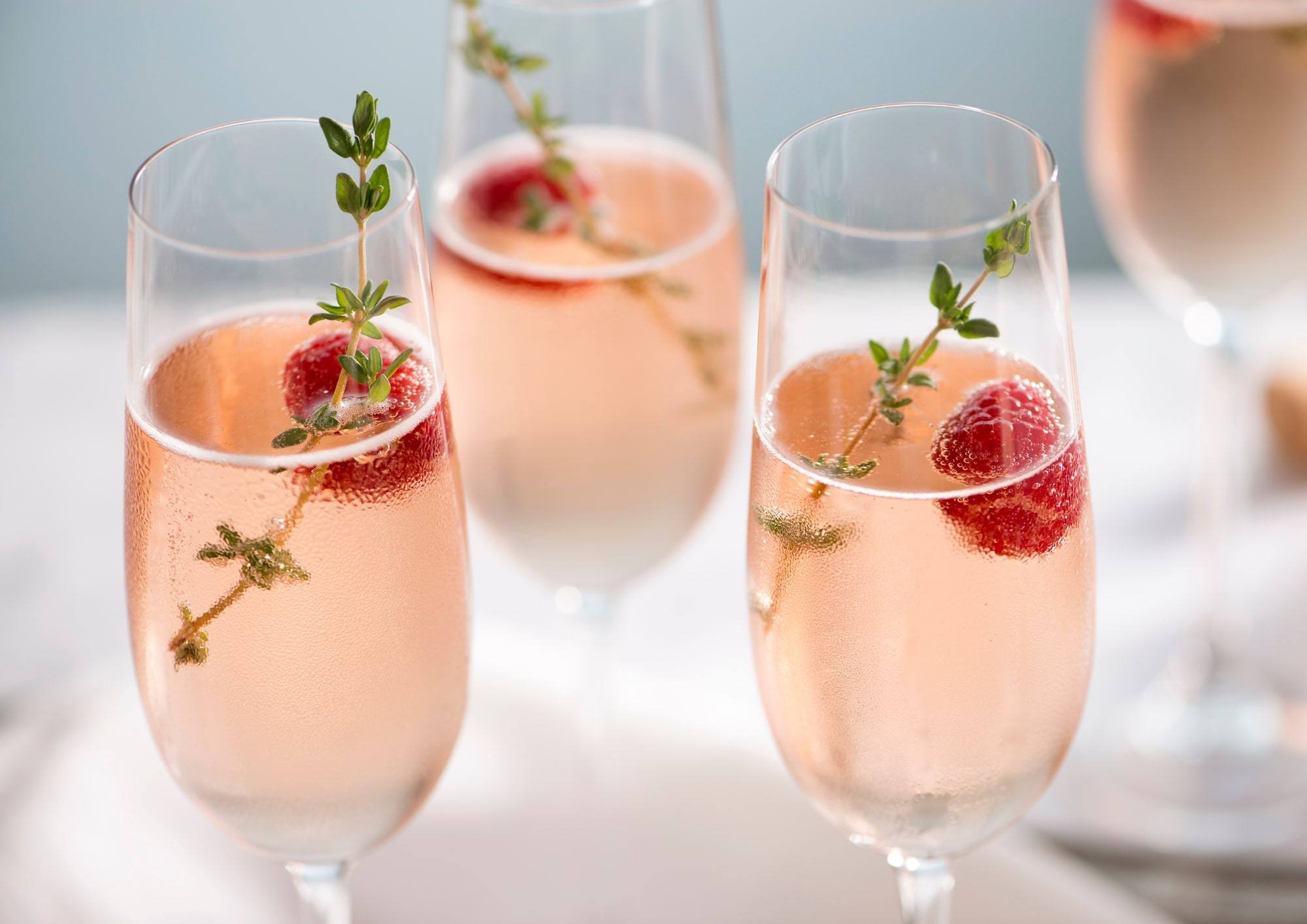 Coupes de champagne rosé garnies de framboises et de thym.