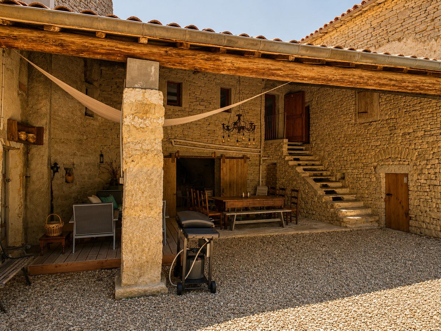 Cour en pierre du hameau au crépuscule, guirlandes tendues au-dessus des tables.